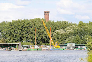 01137_8360 Blick ber die Norderelbe zu den Pontons in Hamburg Entenwerder - Holzhuser, Arbeitsbuden stehen auf den schwimmenden Anlegern, ein Schwimmkran und Barkassen / Schuten haben dort festgemacht. Hinter den Bumen vom Elbpark Entenwerder die Spitze vom Wasserspiel / Wasserturm Hamburg Rothenburgsort. 